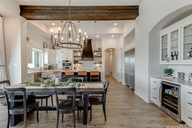 dining space with beverage cooler, arched walkways, beam ceiling, and an inviting chandelier