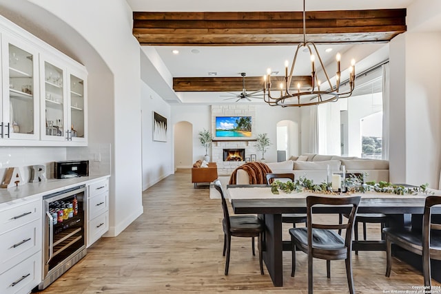 dining area with a warm lit fireplace, beverage cooler, beamed ceiling, and arched walkways