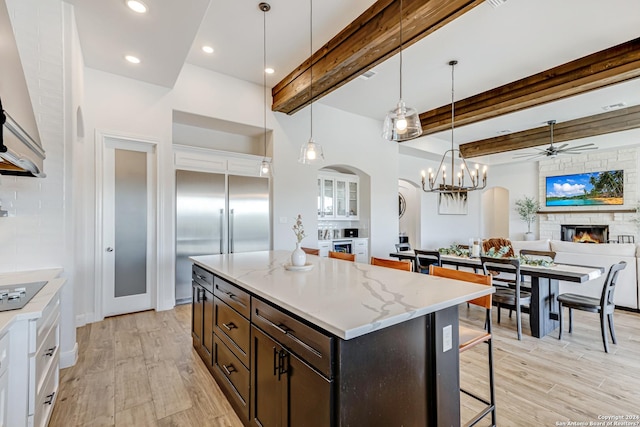 kitchen featuring light wood-type flooring, ceiling fan with notable chandelier, a stone fireplace, and beamed ceiling