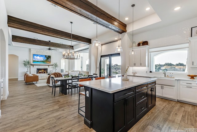 kitchen featuring a stone fireplace, white cabinets, dark cabinetry, a sink, and light wood-style flooring