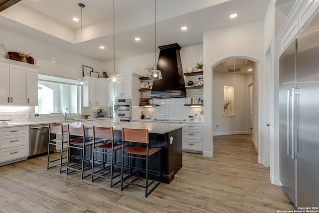 kitchen with arched walkways, open shelves, ventilation hood, white cabinets, and stainless steel appliances