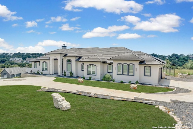 french country inspired facade with a tiled roof, a front yard, a chimney, and concrete driveway