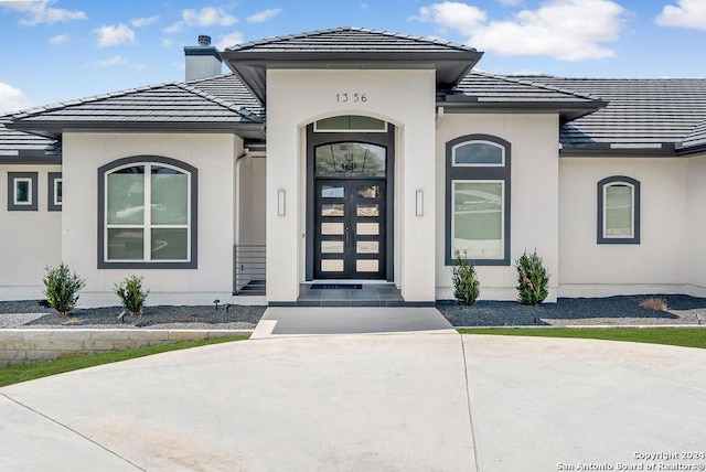 entrance to property with a tiled roof, a chimney, and stucco siding