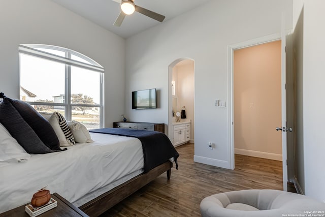 bedroom featuring connected bathroom, arched walkways, baseboards, wood finished floors, and lofted ceiling