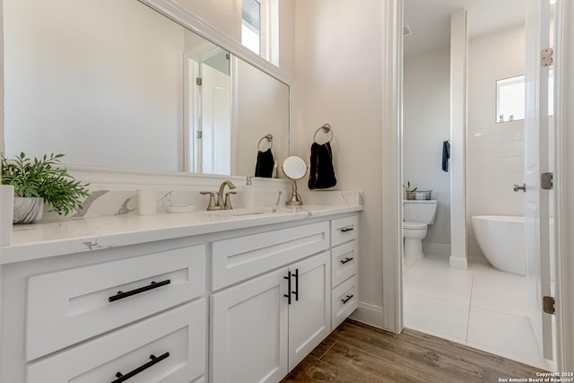 bathroom with vanity, a freestanding tub, wood finished floors, toilet, and baseboards