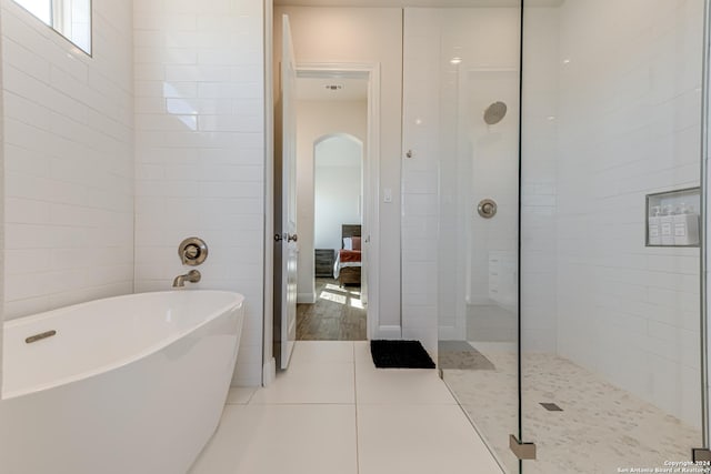 ensuite bathroom featuring connected bathroom, tile patterned floors, a freestanding bath, and a tile shower