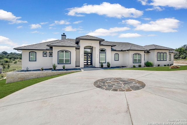 view of front of home featuring curved driveway, a chimney, a tile roof, and stucco siding