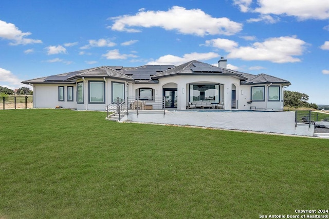 rear view of property with a lawn, roof mounted solar panels, and fence