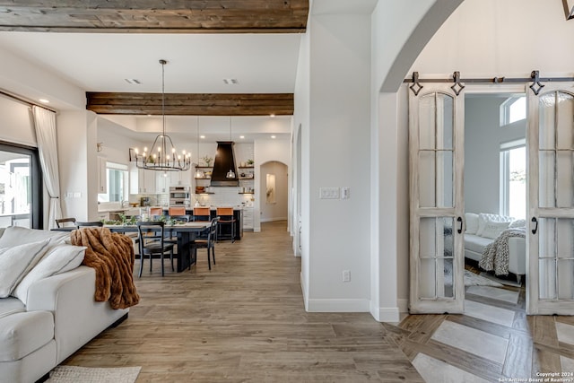 living room featuring light wood-style floors, arched walkways, a chandelier, baseboards, and beamed ceiling