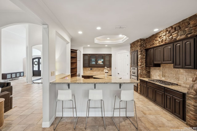 kitchen featuring a breakfast bar, stainless steel gas cooktop, arched walkways, decorative backsplash, and light stone countertops