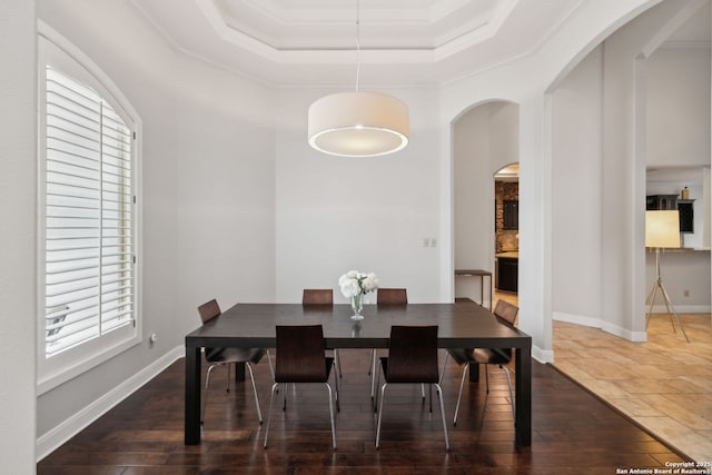 dining space with ornamental molding, a wealth of natural light, a raised ceiling, and arched walkways