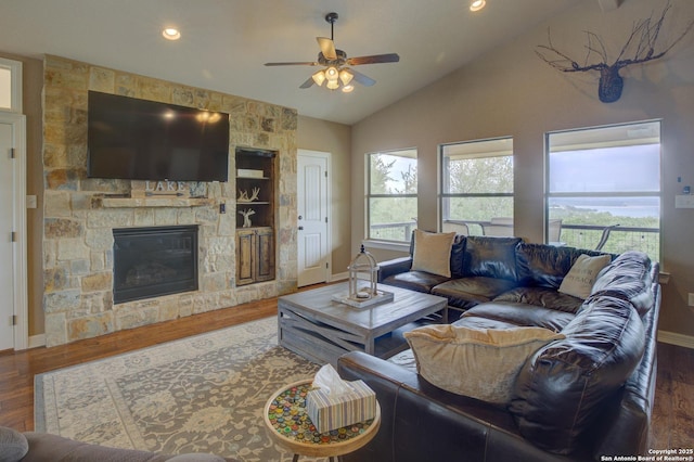 living room with ceiling fan, a stone fireplace, baseboards, wood finished floors, and lofted ceiling