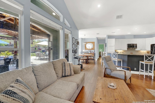living room with plenty of natural light, lofted ceiling, light wood finished floors, and visible vents
