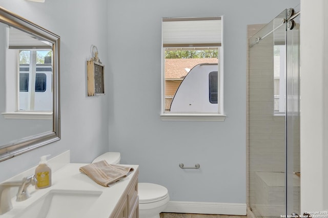 bathroom featuring vanity, baseboards, a shower with door, and toilet