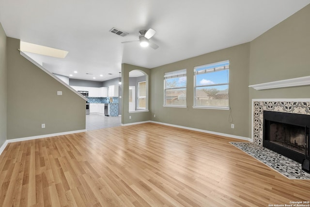 unfurnished living room featuring ceiling fan, light wood-style floors, baseboards, a tile fireplace, and visible vents