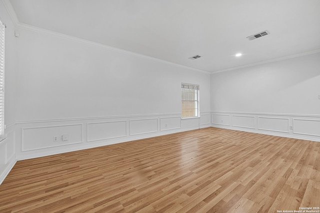 spare room with visible vents, light wood-style floors, crown molding, and wainscoting