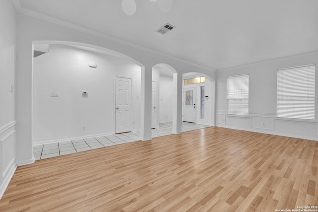 unfurnished living room with crown molding, arched walkways, visible vents, and light wood finished floors