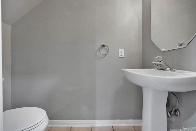 half bath with a sink, baseboards, tile patterned flooring, and toilet