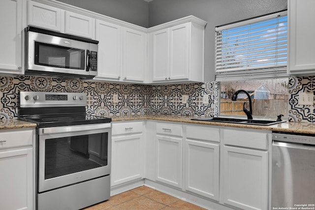 kitchen with white cabinetry, tasteful backsplash, a sink, light tile patterned floors, and stainless steel appliances