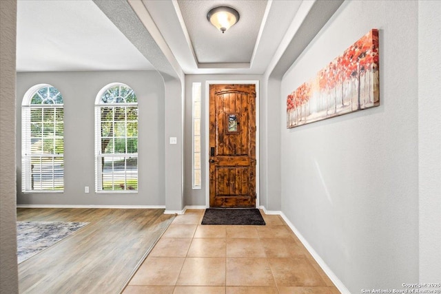 foyer entrance with baseboards, light wood-style flooring, and a tray ceiling