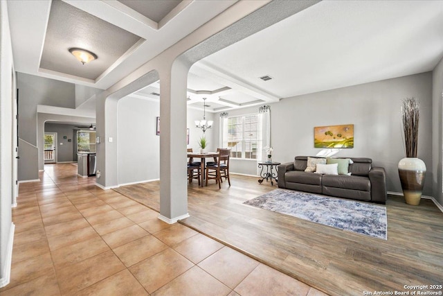 living area featuring arched walkways, baseboards, coffered ceiling, and a chandelier