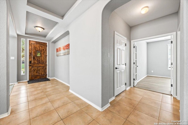 entryway featuring baseboards, arched walkways, and light tile patterned floors