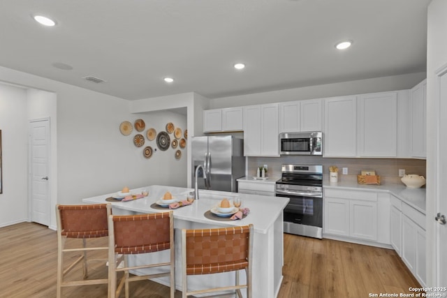 kitchen featuring light countertops, decorative backsplash, stainless steel appliances, and an island with sink