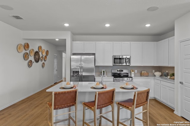 kitchen with visible vents, decorative backsplash, light wood-style floors, a kitchen breakfast bar, and stainless steel appliances