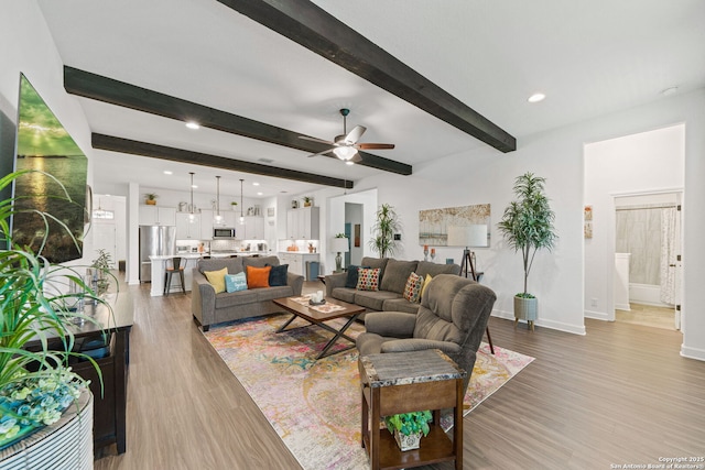 living room with a ceiling fan, recessed lighting, baseboards, light wood-type flooring, and beamed ceiling