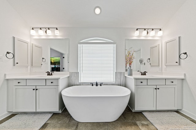 full bath with a sink, wainscoting, a freestanding bath, and two vanities