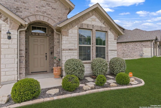 view of exterior entry with a lawn, brick siding, and stone siding