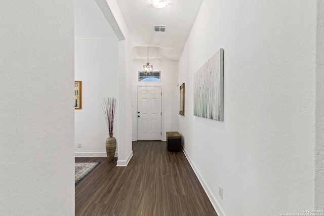 hallway featuring baseboards, dark wood finished floors, a textured wall, and visible vents