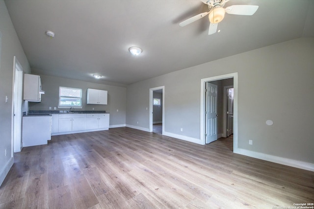 unfurnished living room with baseboards, a ceiling fan, light wood finished floors, and a sink