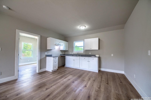 kitchen featuring baseboards, a sink, light wood finished floors, and white cabinets