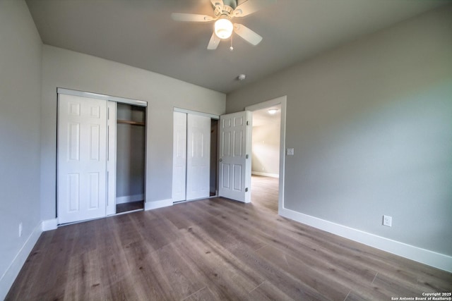 unfurnished bedroom with baseboards, a ceiling fan, dark wood-style flooring, and two closets