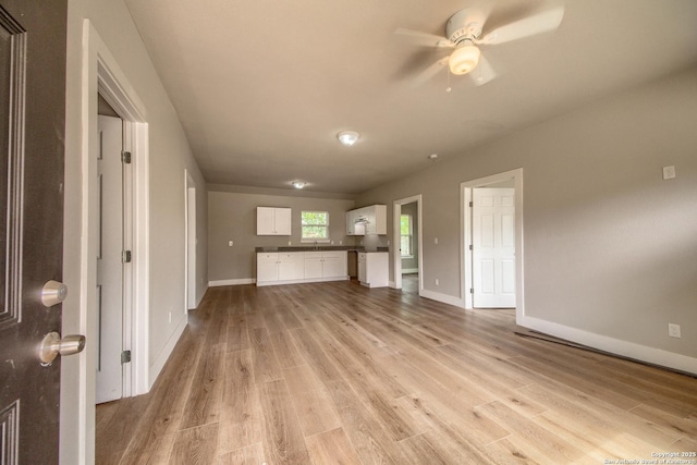 unfurnished living room with light wood-style floors, a ceiling fan, and baseboards
