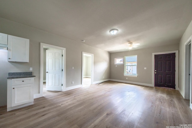 interior space with baseboards, ceiling fan, and light wood-style flooring