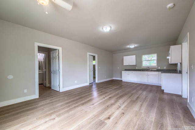 unfurnished living room featuring a ceiling fan, baseboards, a sink, and light wood-style flooring