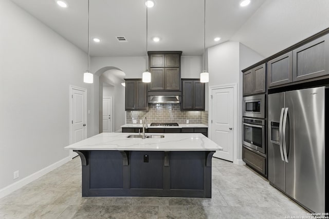 kitchen featuring dark brown cabinetry, a sink, arched walkways, stainless steel appliances, and tasteful backsplash