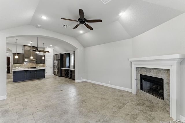 unfurnished living room featuring ceiling fan, visible vents, arched walkways, a fireplace, and vaulted ceiling