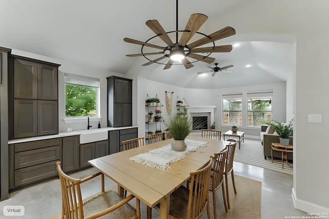 dining area with a ceiling fan, a fireplace with raised hearth, vaulted ceiling, and a wealth of natural light