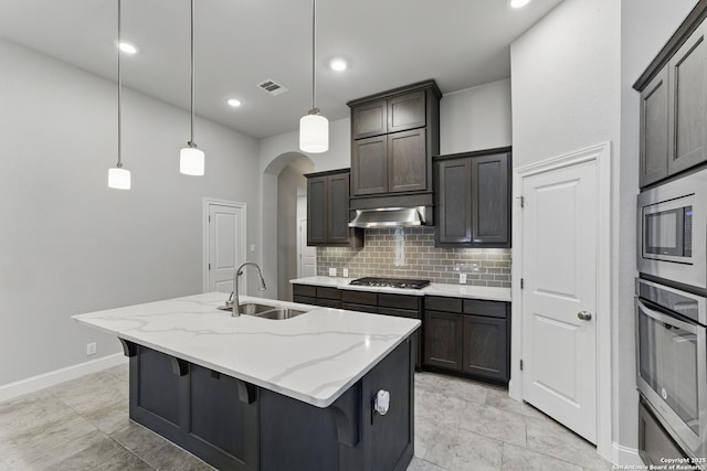 kitchen featuring decorative backsplash, arched walkways, a sink, stainless steel appliances, and an island with sink