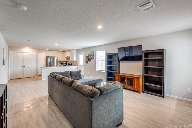 living room featuring baseboards, light wood finished floors, a textured ceiling, and visible vents