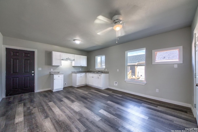 kitchen with baseboards, under cabinet range hood, white cabinets, a ceiling fan, and dark wood finished floors