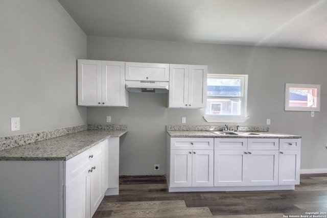 kitchen with dark wood-type flooring, under cabinet range hood, white cabinets, light stone counters, and a sink