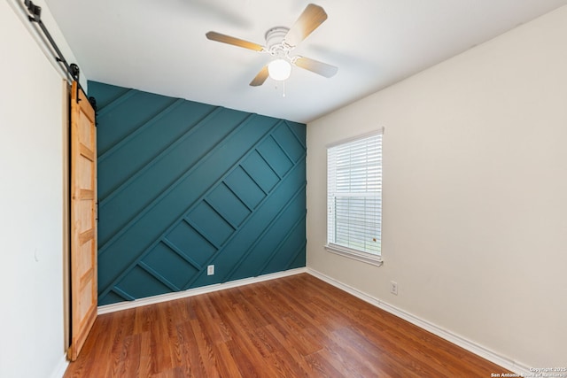 empty room with baseboards, ceiling fan, a barn door, and wood finished floors