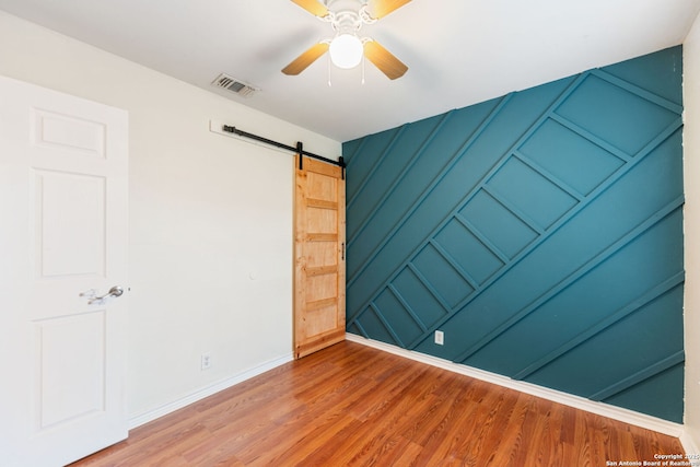 unfurnished room with ceiling fan, visible vents, a barn door, wood finished floors, and baseboards