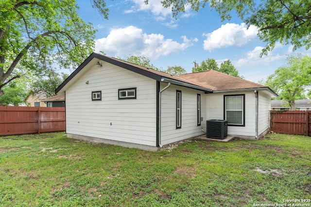 back of house featuring a fenced backyard, roof with shingles, central AC, and a yard