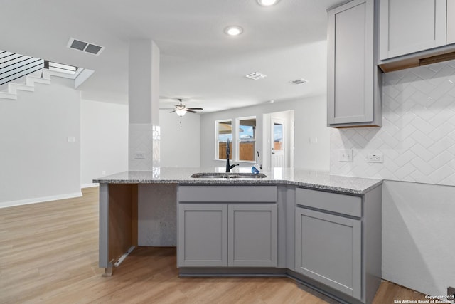 kitchen with gray cabinetry, decorative backsplash, a sink, and visible vents