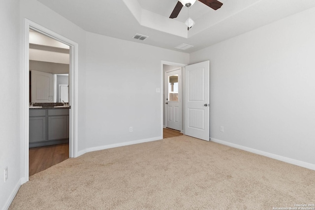 unfurnished bedroom featuring a sink, carpet, baseboards, a tray ceiling, and visible vents